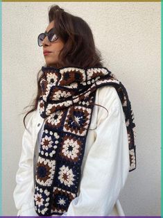 a woman wearing glasses and a crocheted scarf with flowers on it is standing in front of a white wall