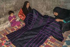 two women and a child are sitting on the floor covered by blankets in an alleyway