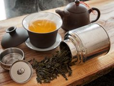 a cup of tea next to some metal containers on a wooden table with steam coming out of it