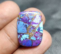 a close up of a person's hand holding a ring with blue and purple stones on it