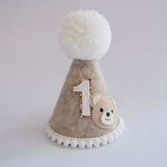 a small felt hat with a teddy bear on the front and number 1 on the back