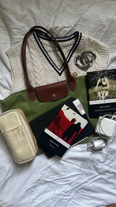 the contents of a purse laid out on top of a white bed with a handbag