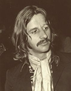 a black and white photo of a man with long hair, wearing a suit and tie