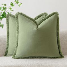 two green pillows sitting on top of a white couch next to a potted plant