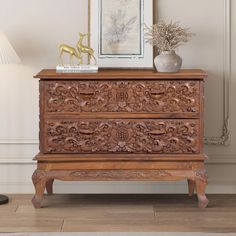 an ornate wooden chest of drawers next to a lamp and pictures on the wall behind it