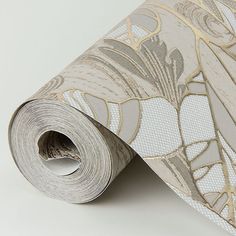 a white and gold wallpaper with floral design on the bottom half of it, next to a roll of tape