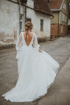 a woman is walking down the street in a white wedding dress with long sleeves and an open back