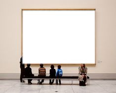 four people sitting on a bench in front of a large white board hanging from the wall