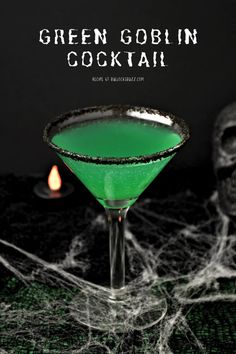 a green cocktail sitting on top of a table next to a halloween pumpkin and spooky spider web