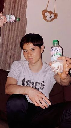 a young man sitting on a couch holding two bottled water bottles