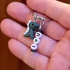 a hand holding a key chain with a dinosaur on it's side and the word love spelled in small letters