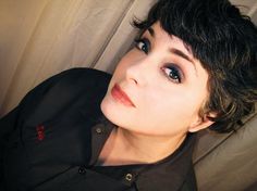 a close up of a person wearing a black shirt and blue eyeshadow with short hair