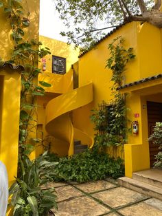 a yellow building with stairs leading up to the top floor and plants growing all around it