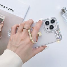 a woman holding an iphone case with some rings on it and a book next to her