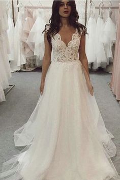 a woman standing in front of a rack of wedding dresses