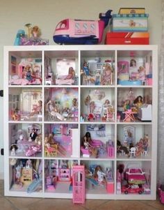 a white bookcase filled with lots of barbie dolls and toys on top of it