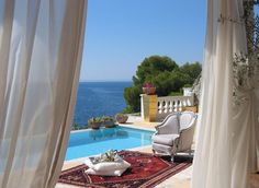 an outdoor area with a couch, chair and table next to a pool overlooking the ocean