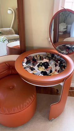 a round mirror sitting on top of a wooden table next to a stool and ottoman