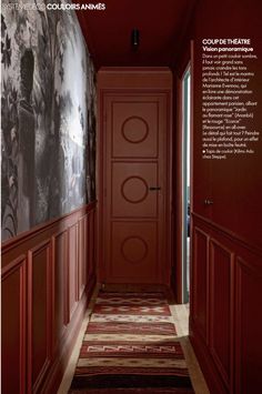 an empty hallway with red painted walls and wooden paneling on the wall, leading to another room