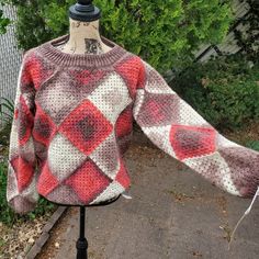 a sweater on a mannequin with trees in the background and bushes behind it