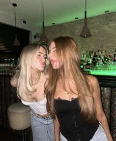 two beautiful young women standing next to each other in front of a bar with green lights