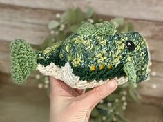 a green crocheted fish sitting on top of a wooden table next to a plant