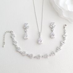 a necklace, bracelet and earring set on a white surface with a flower in the background