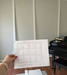 a person holding up a piece of paper with drawings on it in front of a piano