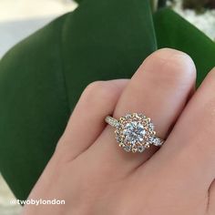 a woman's hand with a diamond ring on top of her finger, next to a green plant