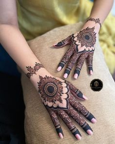 two hands with henna designs on them sitting on a cushion next to each other