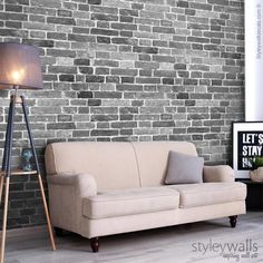 a living room with a couch and lamp in front of a brick wall that has been painted gray