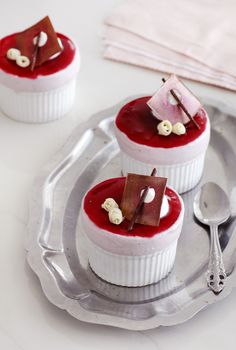 three small desserts on a silver plate with spoons and napkin in the background