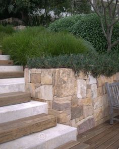 a wooden bench sitting next to a stone wall and green grass growing on top of it