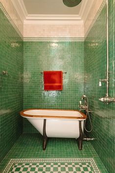 a green tiled bathroom with a bathtub, shower head and red towel hanging on the wall