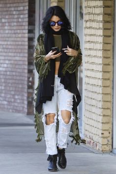 a woman in ripped white jeans is looking at her cell phone while walking down the street