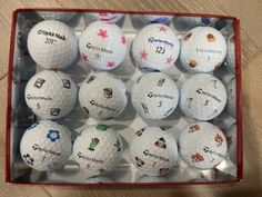 a dozen golf balls in a red box on a wooden floor with the names of each team