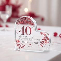 a glass heart shaped table number holder with leaves on it and the number forty written in red