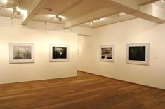 an empty room with paintings on the wall and wooden floors in front of white walls