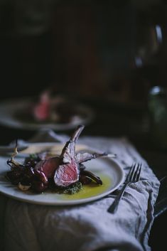 a white plate topped with meat on top of a table next to a fork and knife