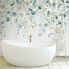 a white bath tub sitting in front of a wall with leaves painted on the walls