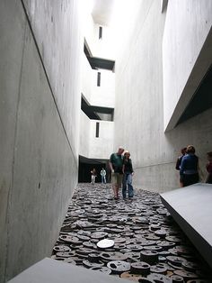 several people are walking in an open space between two concrete buildings, one with circular cutouts on the floor