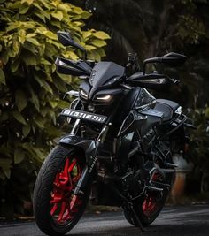 a black motorcycle parked on the street next to some bushes and trees with red rims