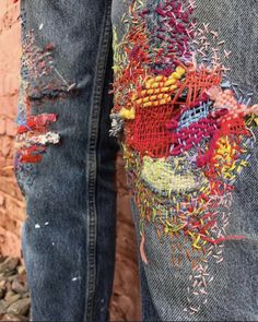 someone is standing in front of a brick wall with colorful thread work on their jeans