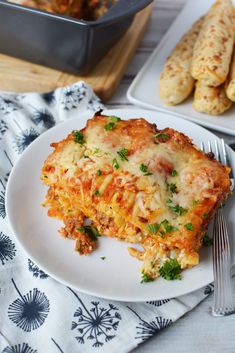 a white plate topped with lasagna next to a casserole dish and silverware