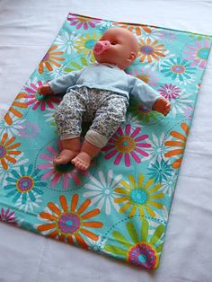 a baby doll laying on top of a colorful flowered mat in the middle of a bed