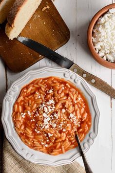 a white plate topped with pasta covered in sauce and parmesan cheese next to bread