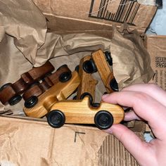 a wooden toy car is being held by someone's hand in a cardboard box