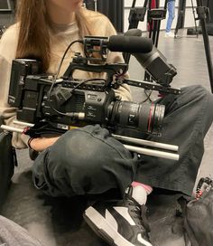 a woman sitting on the ground with a camera in front of her and another person behind her