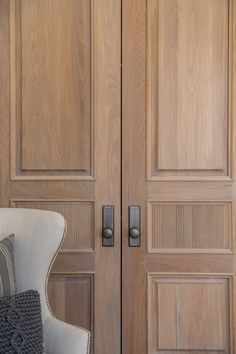 an upholstered chair sits in front of two wooden doors with decorative knobs