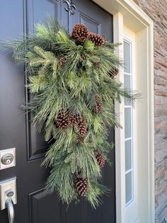 a pine cone wreath on the front door of a house with evergreen cones hanging from it